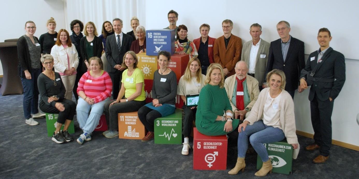 Gruppenfoto von 24 Mitwirkenden der Heidekreis-Bildungskonferenz 2023, die auf und um bunte Pappwürfel mit den 17 Nachhaltigkeitszielen postiert sind.
