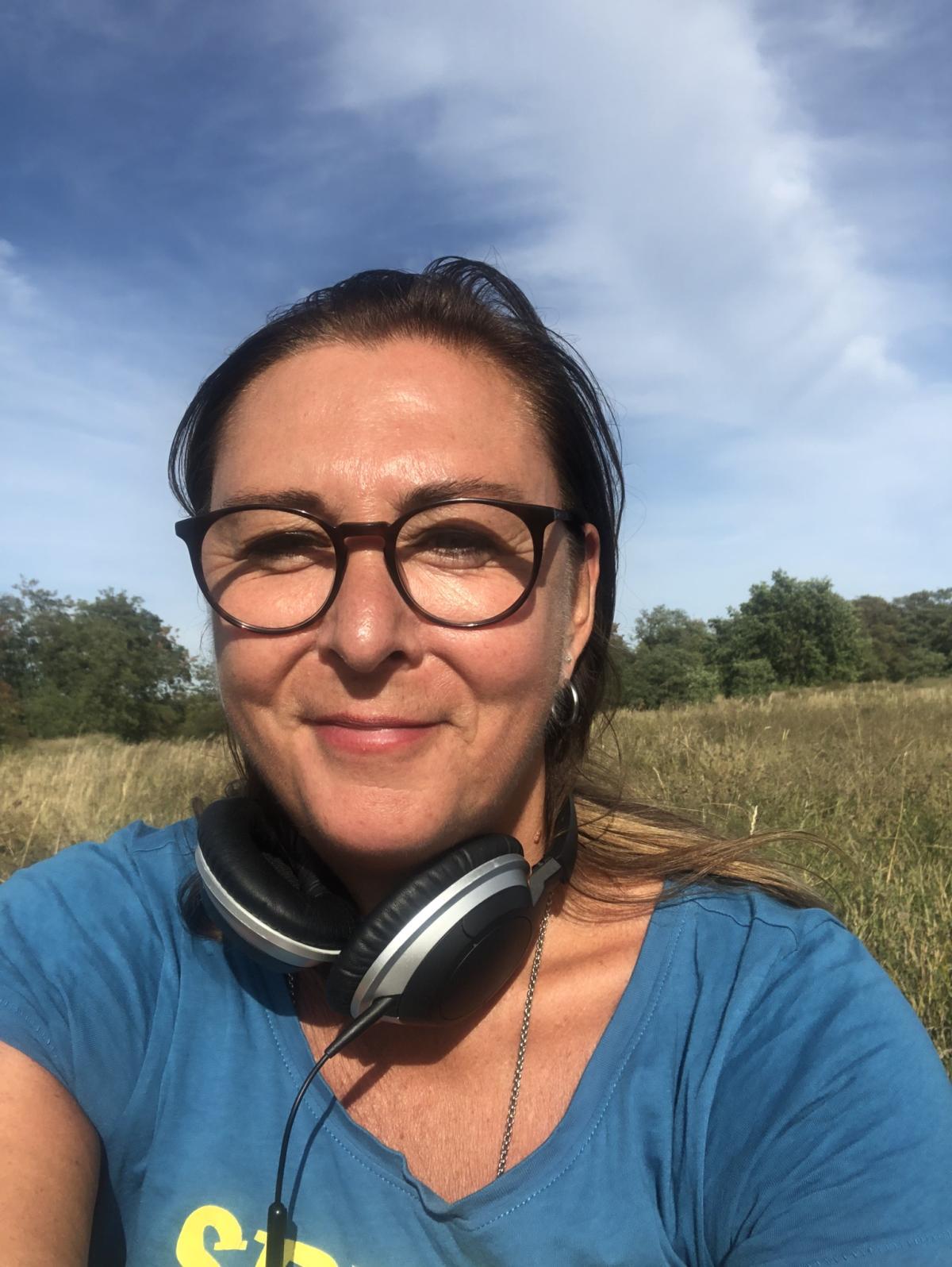 Foto von Elle Langer, einer weißen Frau mit Brille und braunen Haaren, draußen vor einem blauen Himmel